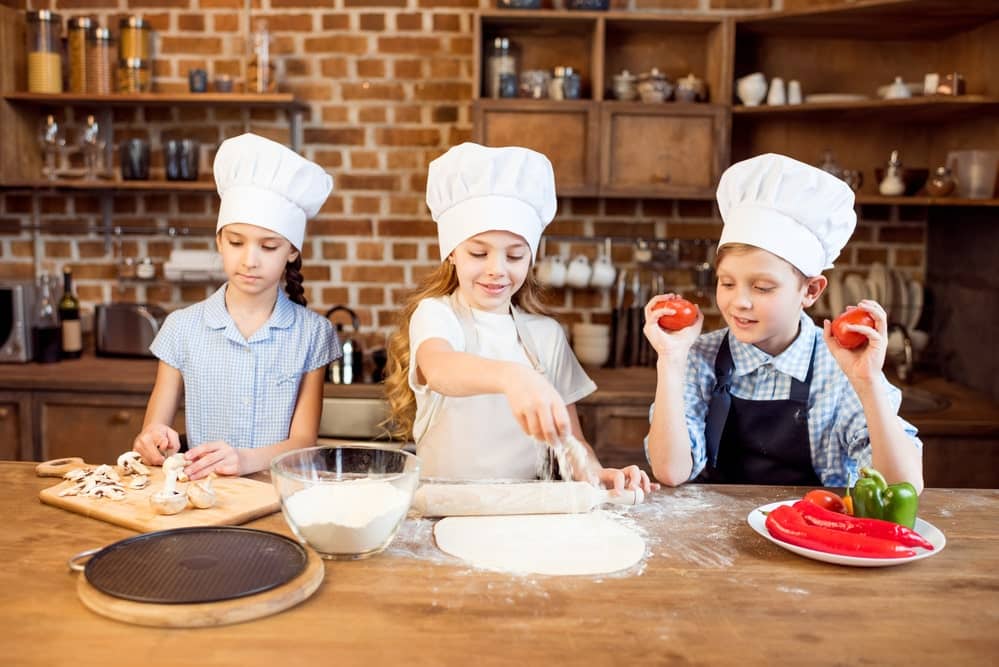 Three kids in the kitchen making pizza
