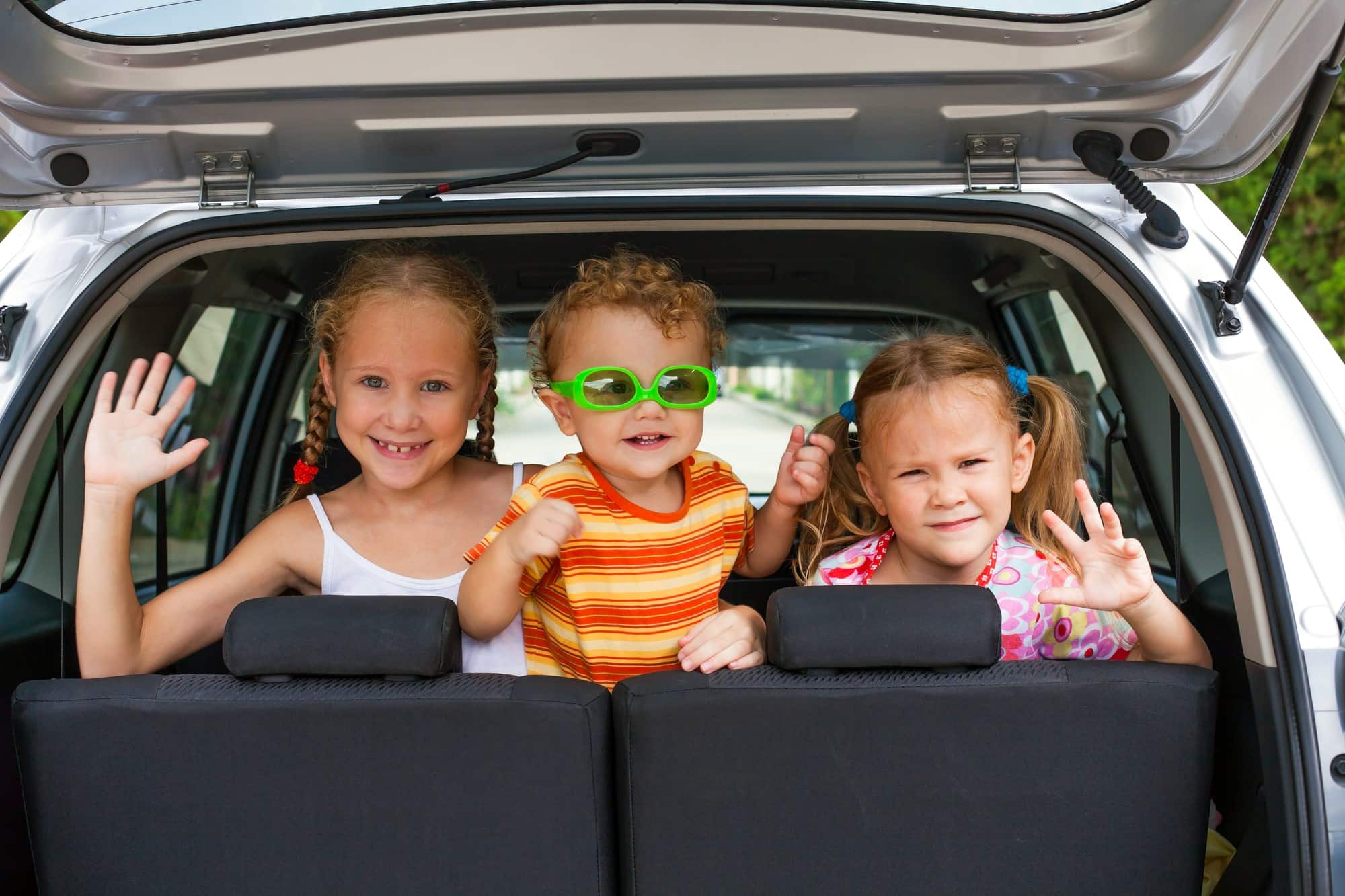 Three kids looking at the back of a car