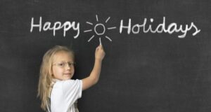 Female student in front of a blackboard that says "Happy Holidays."