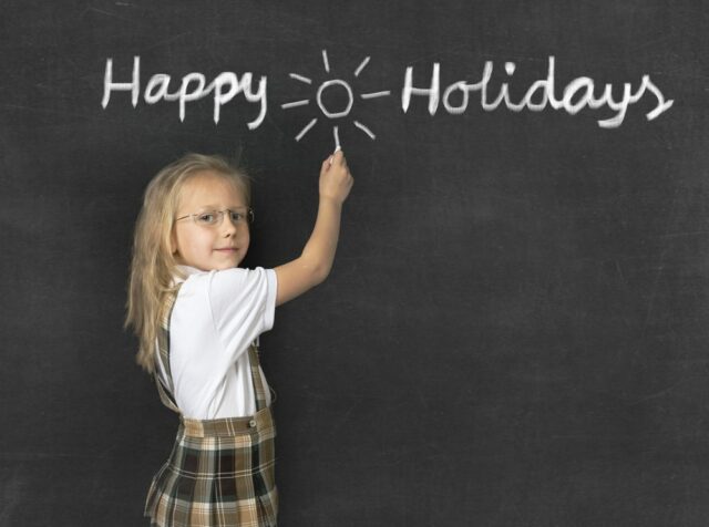 Female student in front of a blackboard that says "Happy Holidays."