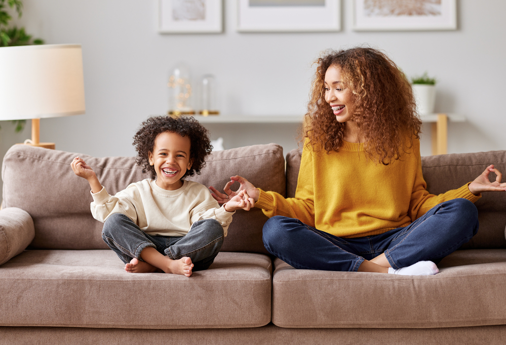 Happy afro american family mother and son in lotus pose meditating together in living room at home