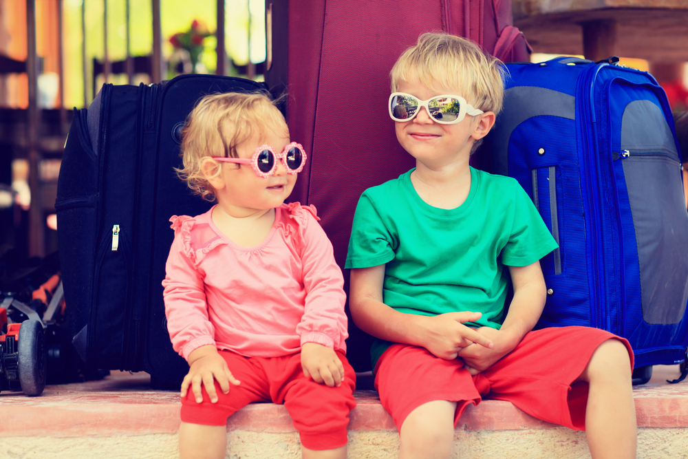 Little boy and toddler girl sitting on suitcases, ready to travel.